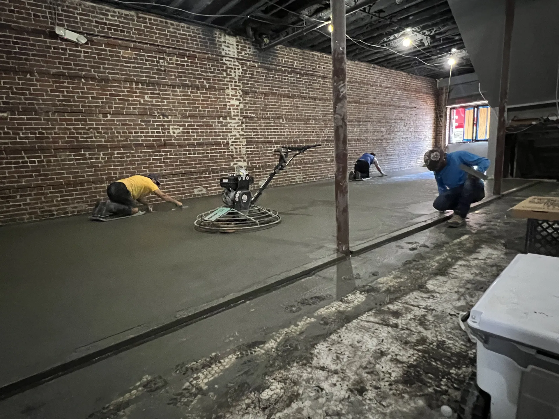 Concrete crew finishing a commercial interior floor slab in a brick building