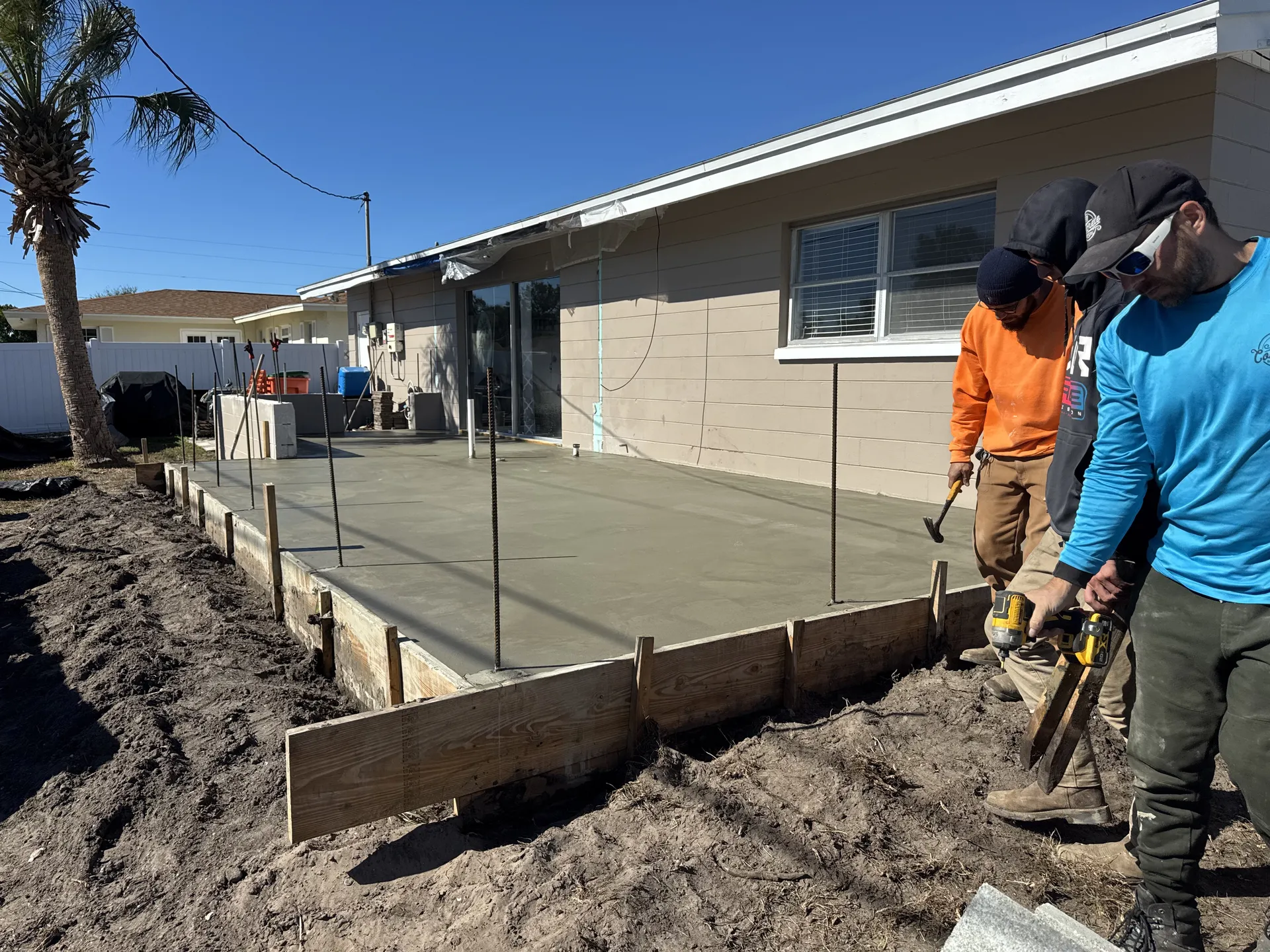 Crew finishing a large concrete patio slab behind a residential home