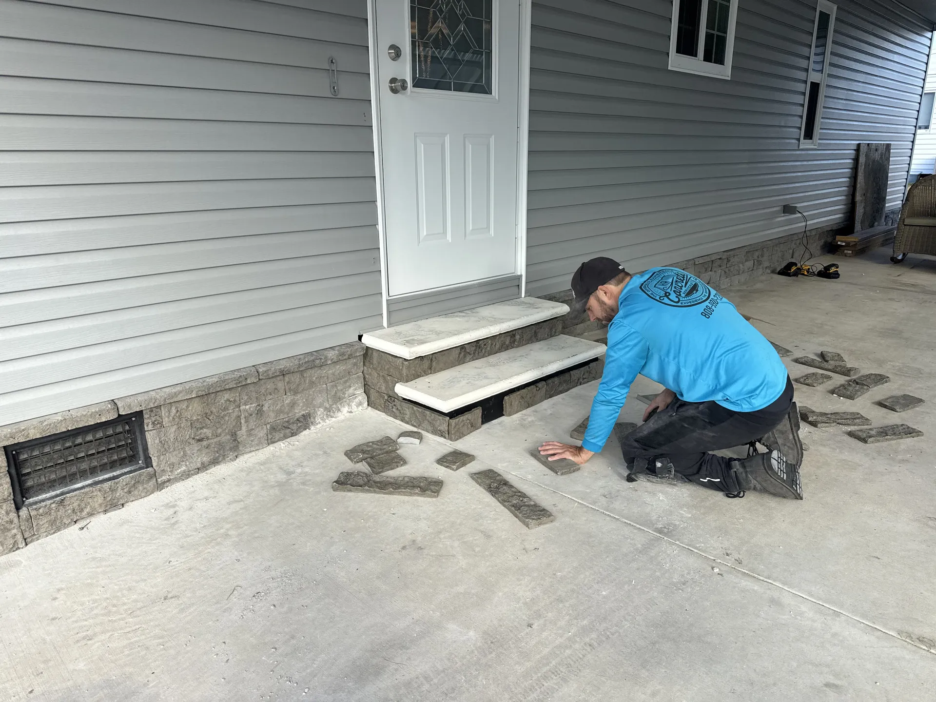 Worker installing stone veneer on concrete front entry steps